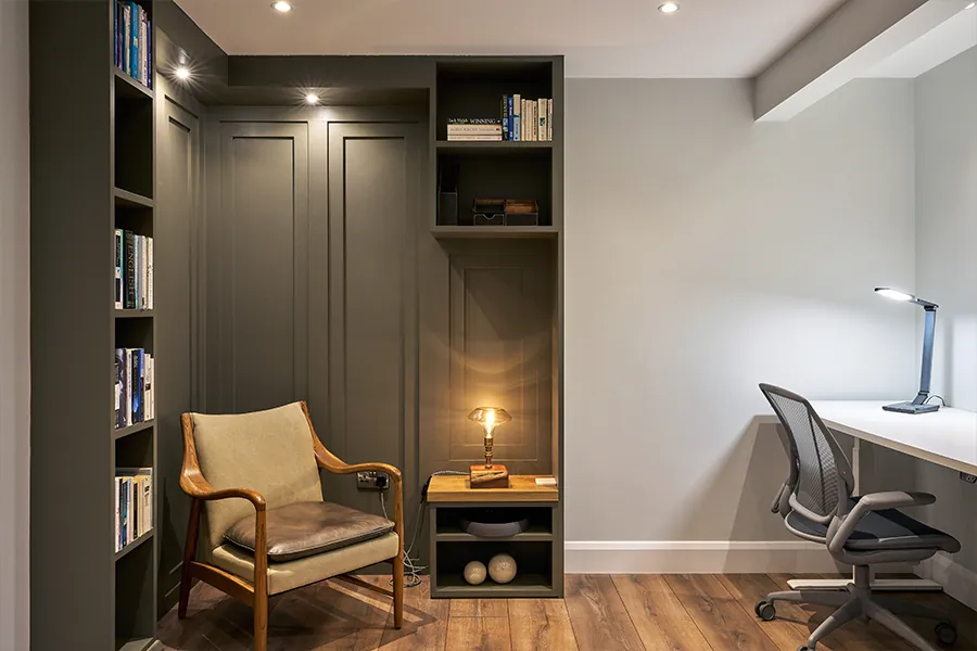 A home office interior with dark built-in shelving, a leather armchair and a desk